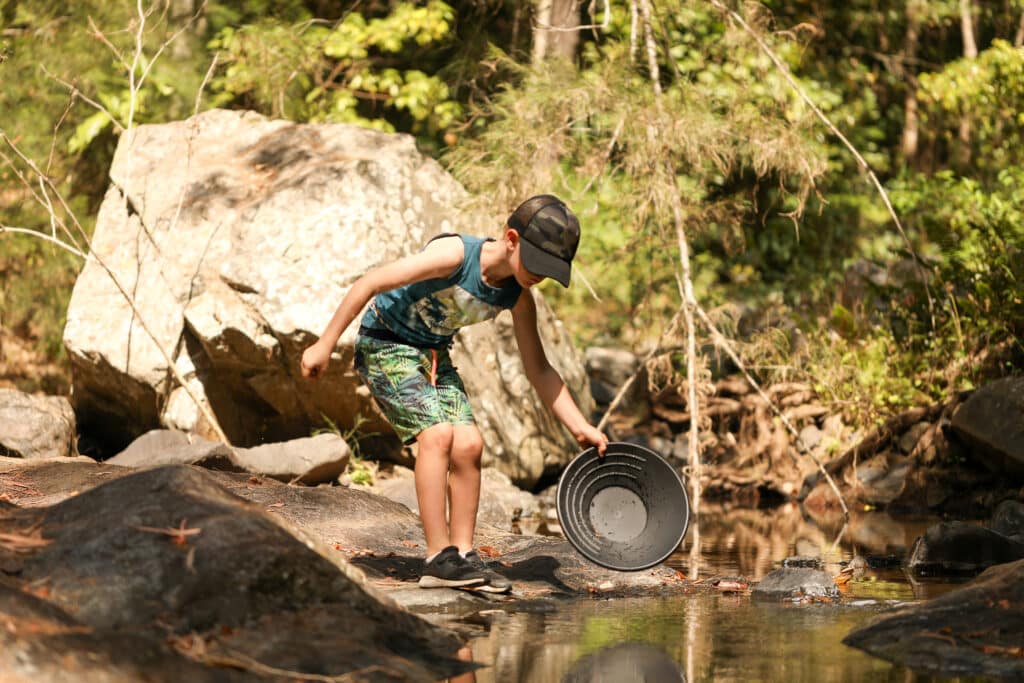 Young boy using pan to search for gold in creek, rural Australia